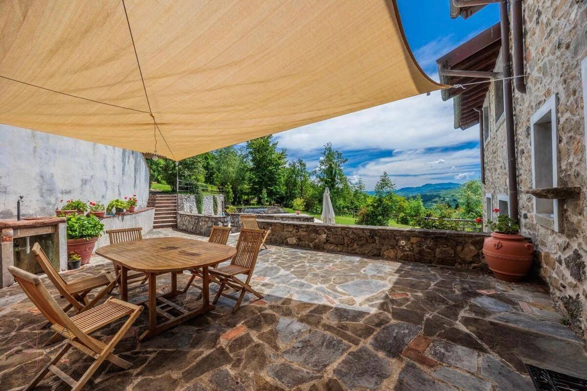 Geräumige Steinterrasse mit Holztisch und Stühlen, bietet einen weiten Blick in die Natur.