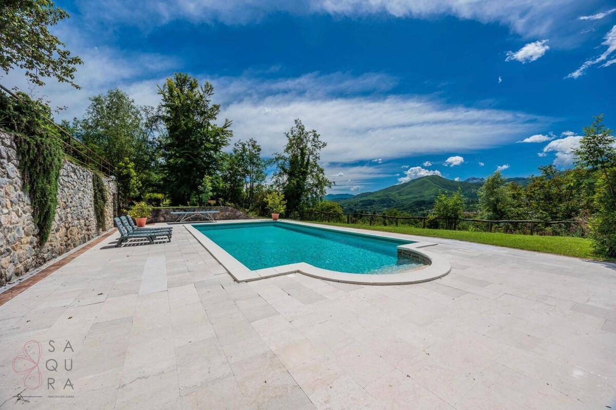 Eleganter Swimmingpool umgeben von einer hellen Terrasse mit weitem Blick in die Natur.