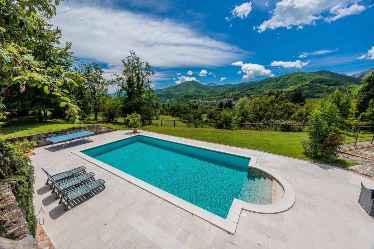 Großer Swimmingpool mit Liegestühlen und Panoramablick auf die umliegenden Berge.