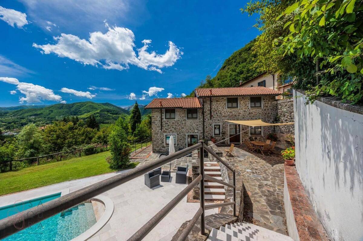 Außenbereich mit Pool, Steinterrasse und einem traditionellen Steinhaus im Hintergrund.