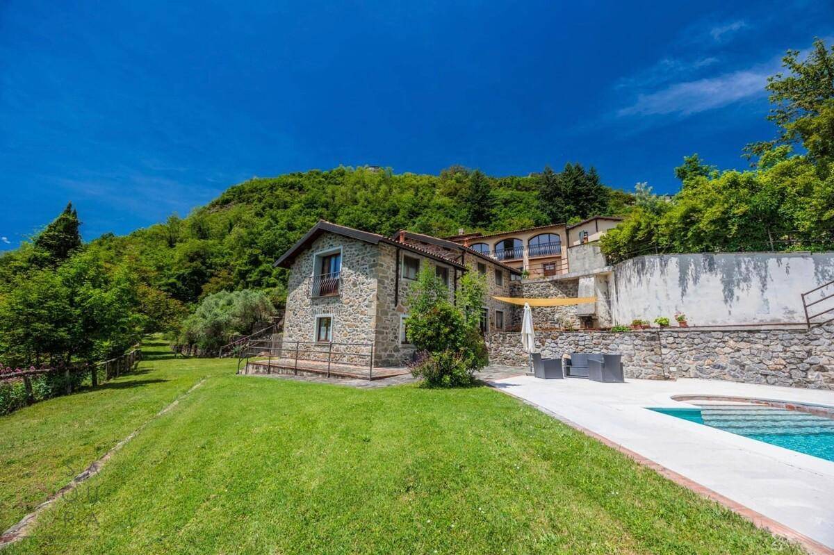 Weitläufiger Gartenbereich mit Rasenfläche, einem Pool und einem traditionellen Steinhaus im Hintergrund.