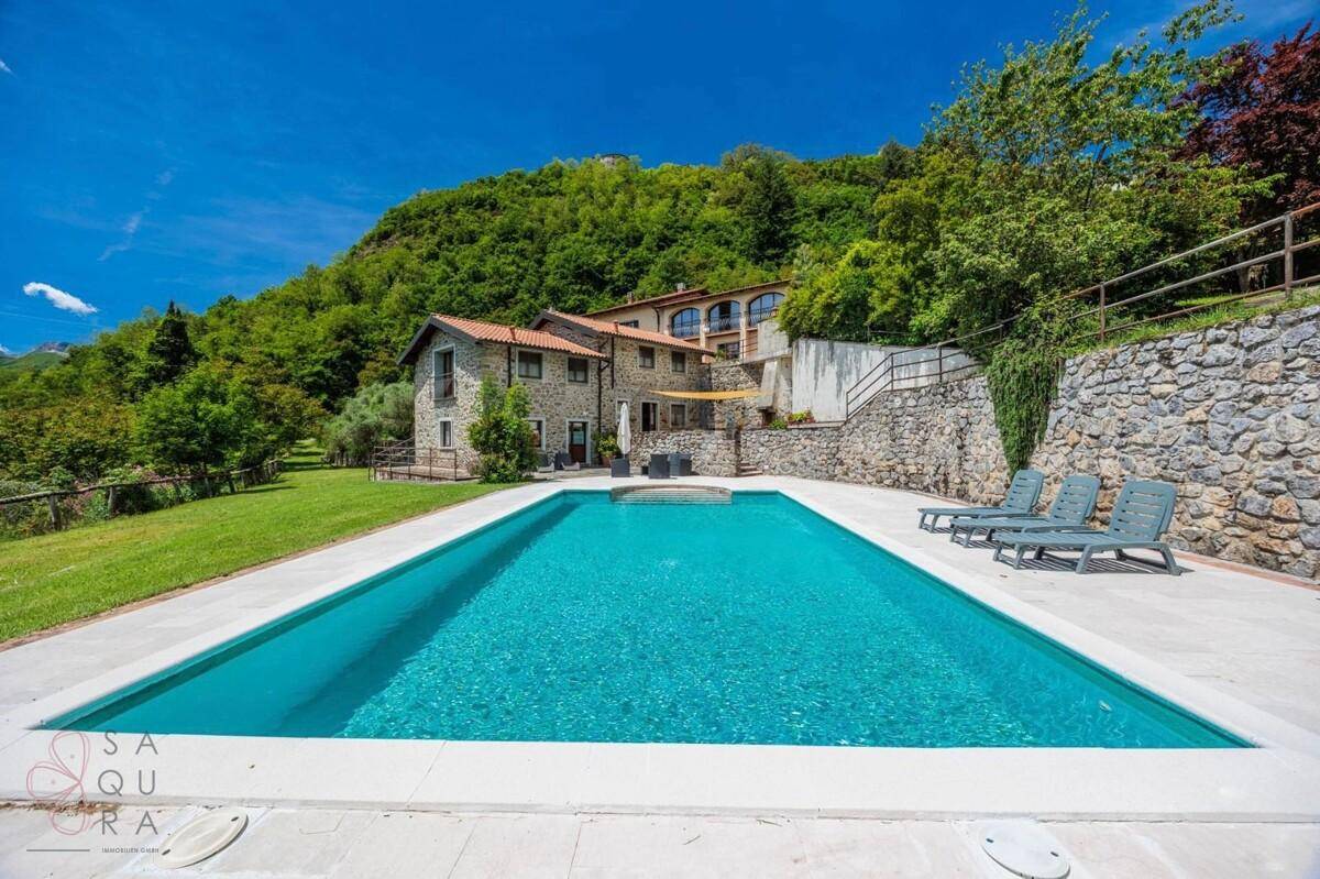 Weitläufiger Poolbereich mit Liegestühlen und Blick auf das traditionelle Steinhaus und die Berge.