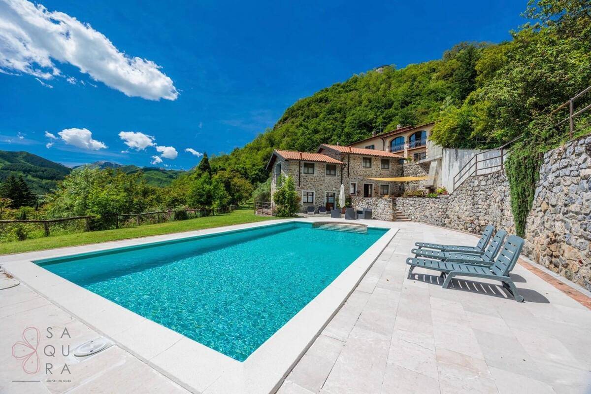 Idyllischer Poolbereich mit Liegestühlen und Blick auf das charmante Steinhaus und die Landschaft.