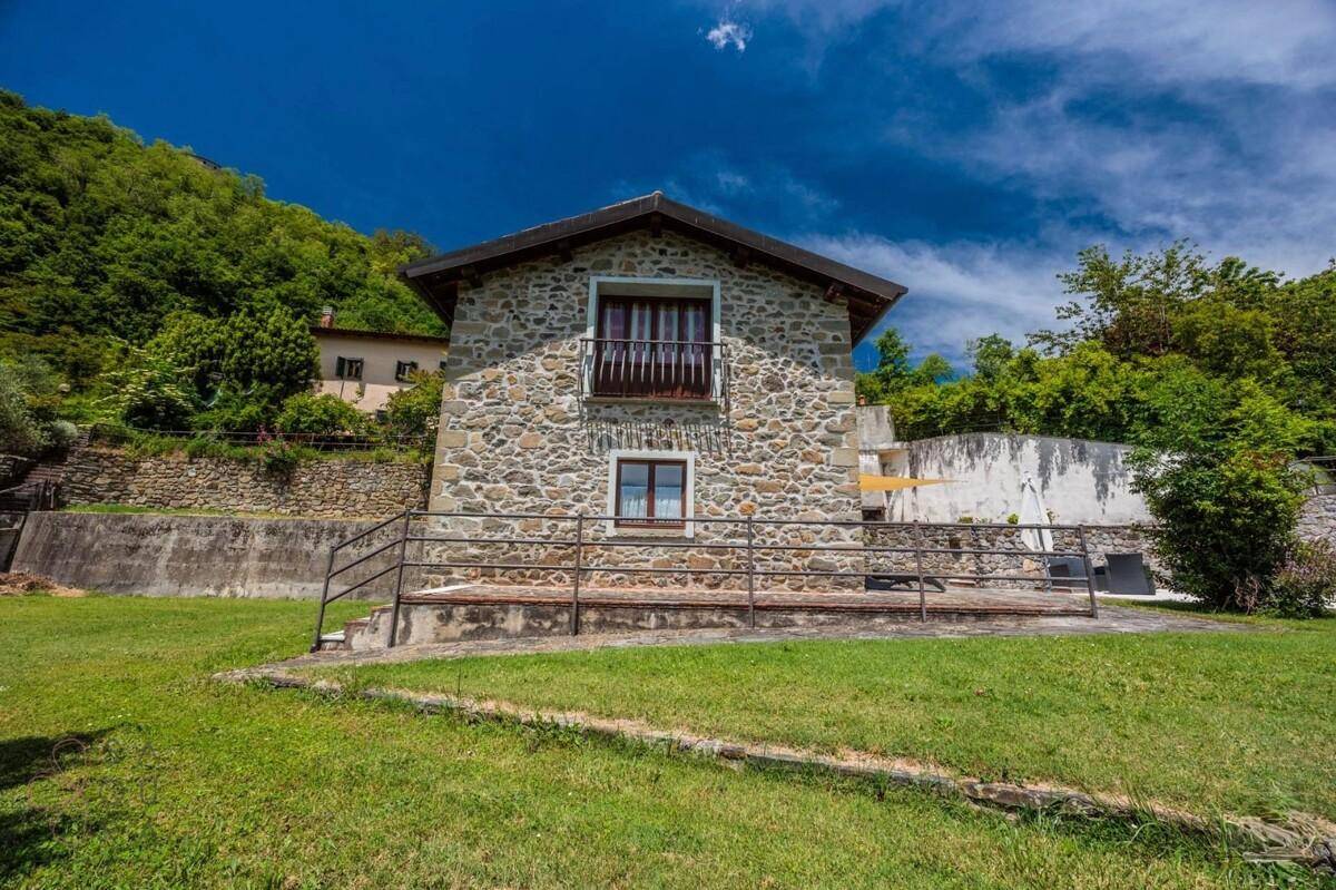 Traditionelles Steinhaus mit kleinem Balkon und rustikalem Geländer vor einer grünen Hügellandschaft.