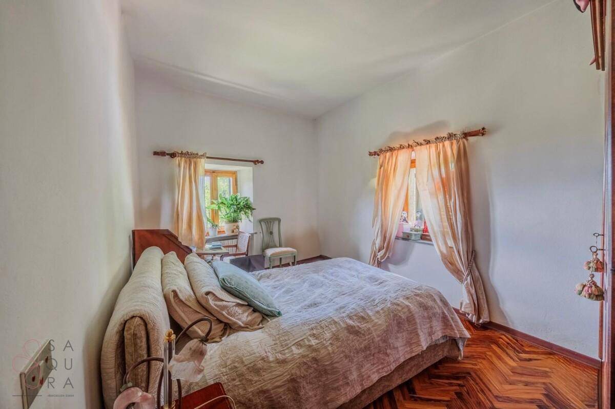 Gemütliches Schlafzimmer mit Doppelbett, Fischgrätparkett und hellen Vorhängen.
