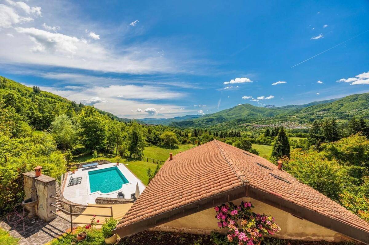 Panoramablick auf ein Hausdach, einen Pool und die weite, grüne Hügellandschaft unter blauem Himmel.