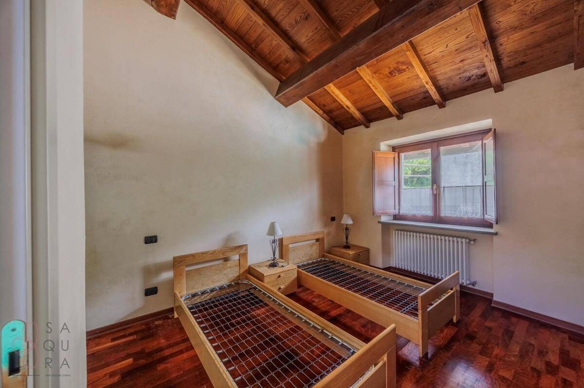 Schlafzimmer mit zwei Einzelbetten, Holzbalkendecke und dunklem Holzboden, hell durch ein Fenster.