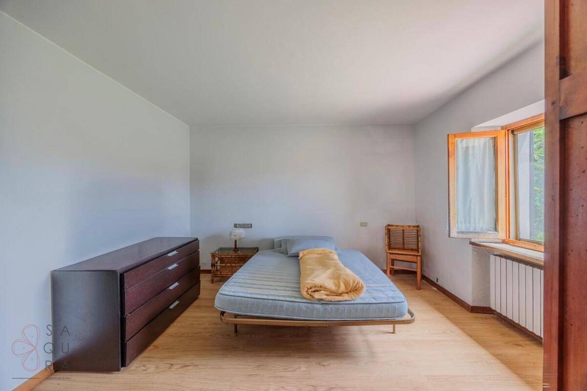 Schlichtes Schlafzimmer mit hellem Holzboden, einem Einzelbett und einem Fenster, das viel Licht hereinlässt.