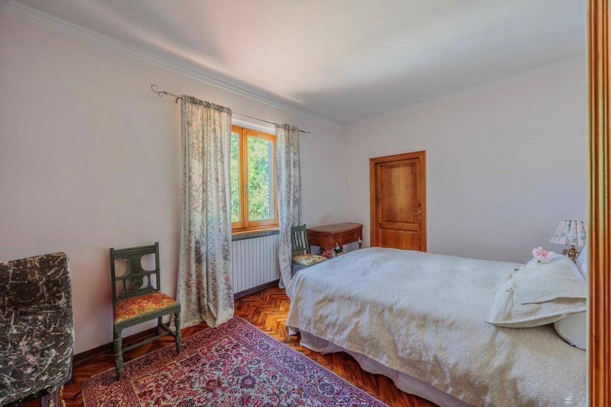 Helles Schlafzimmer mit Doppelbett, Fischgrätparkett und einem Fenster mit Blick ins Grüne.