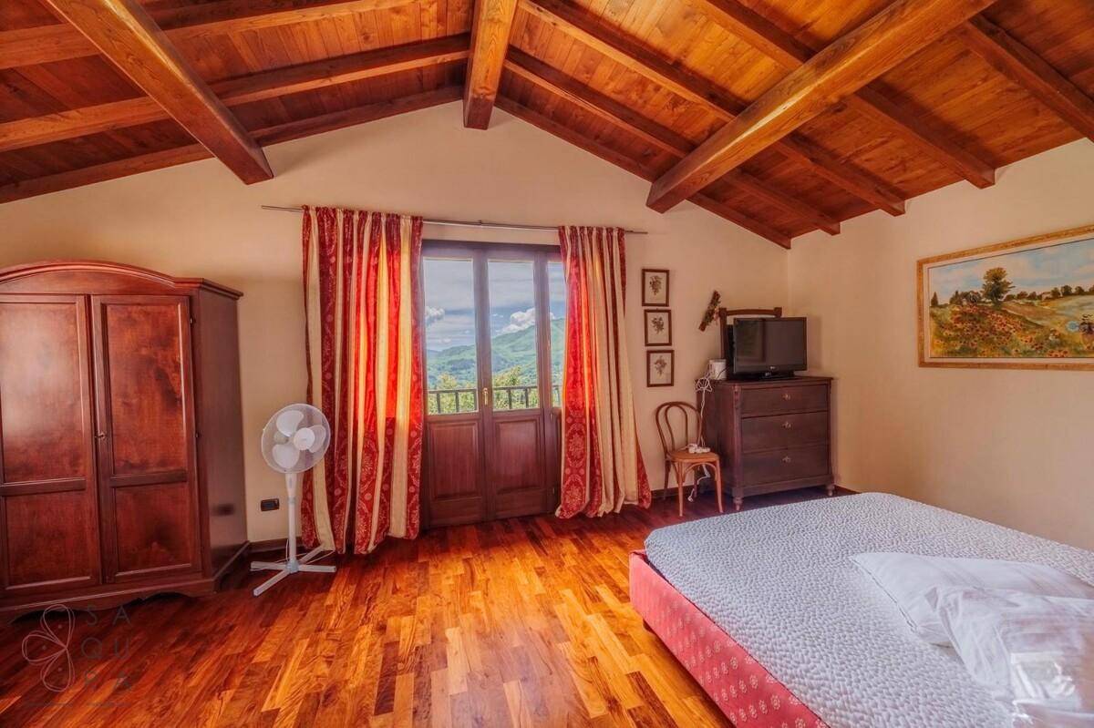Schlafzimmer mit Holzbalkendecke, dunklem Holzboden und Zugang zu einem französischen Balkon mit Bergblick.