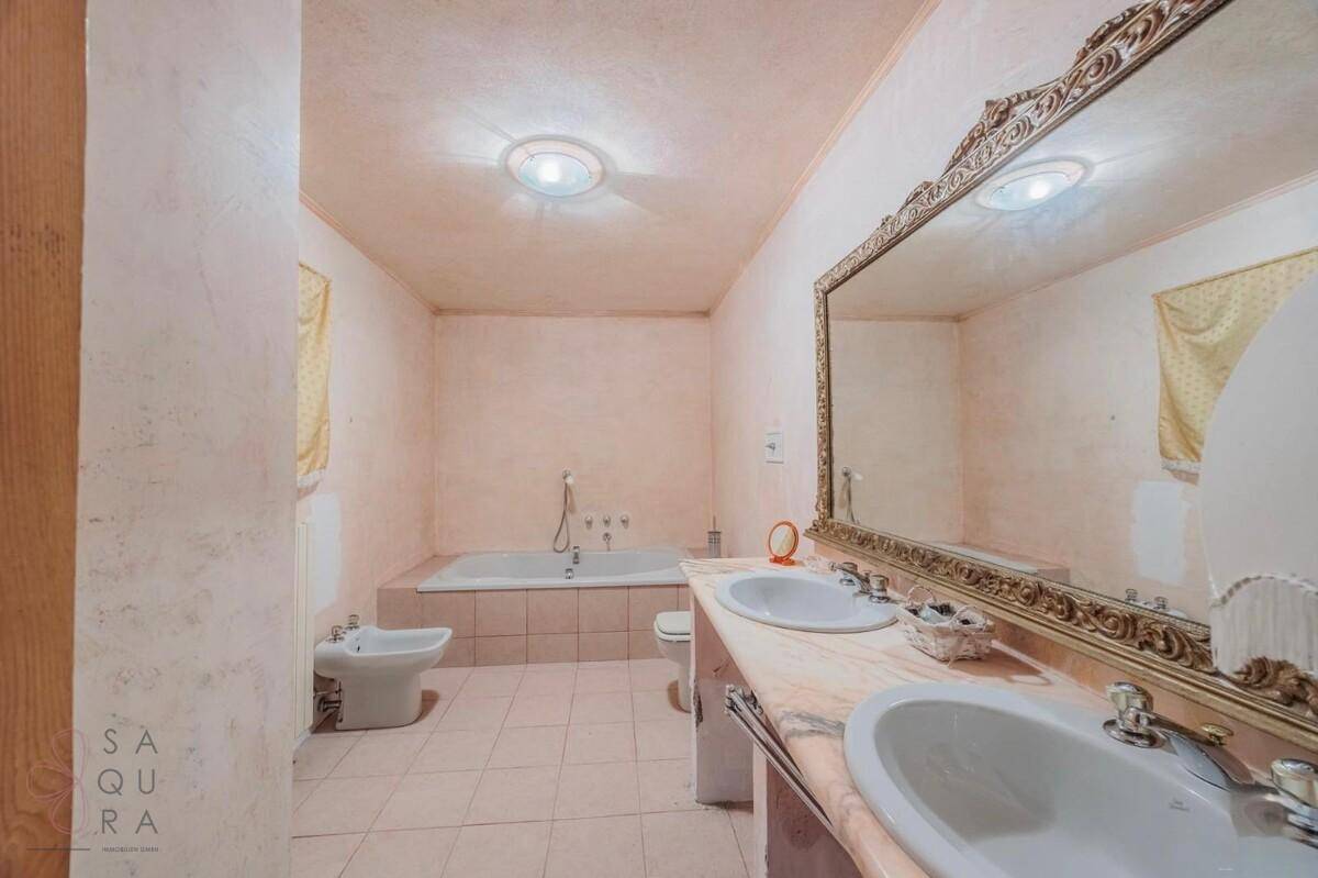 Geräumiges Badezimmer mit Badewanne, Bidet, Doppelwaschbecken und einem großen, verzierten Spiegel.
