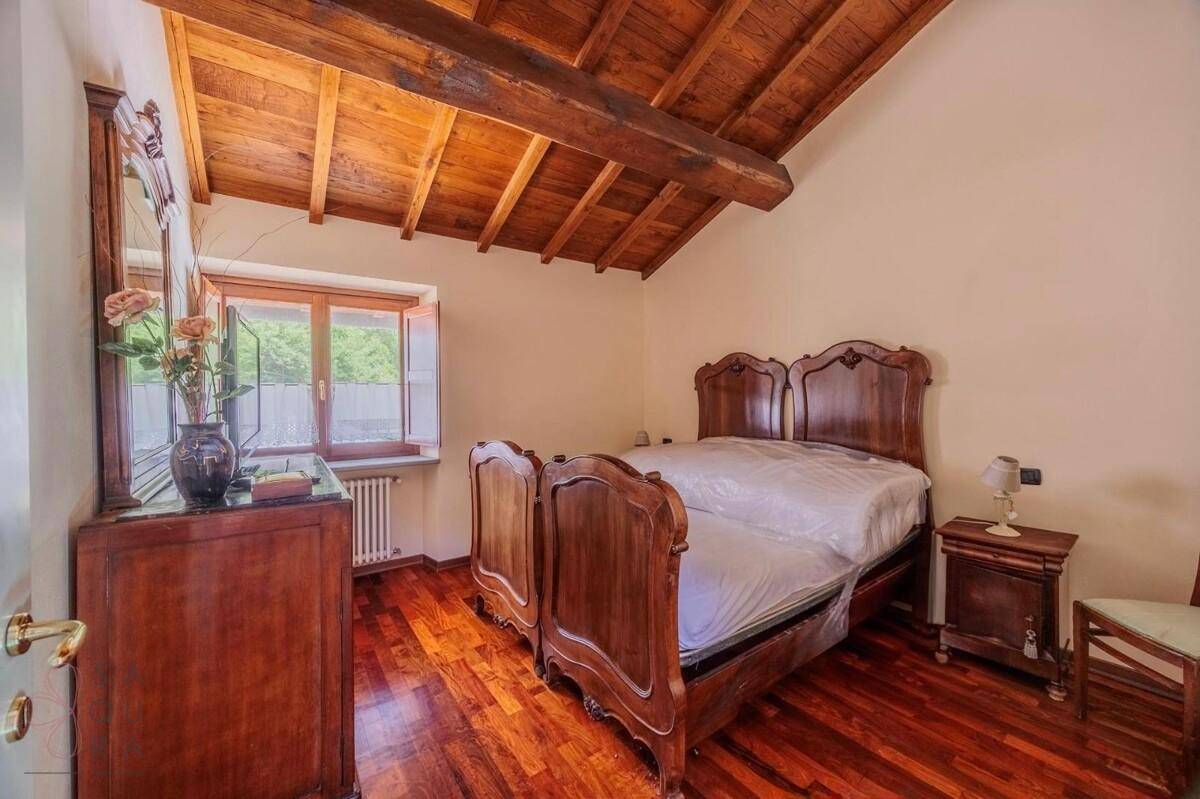 Rustikales Schlafzimmer mit Holzbalkendecke, dunklem Holzboden und einem klassischen Doppelbett.
