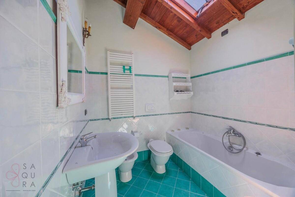 Helles Badezimmer mit Badewanne, Bidet, beheiztem Handtuchhalter und einem Dachfenster unter Holzbalken.