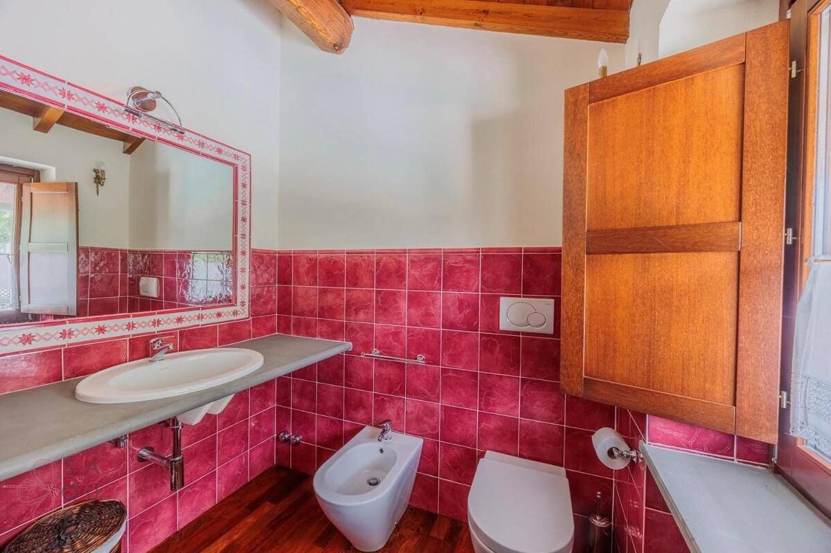 Badezimmer mit rotem Fliesensockel, Holzboden, Waschbecken, Bidet und einem Fenster mit Holzläden.