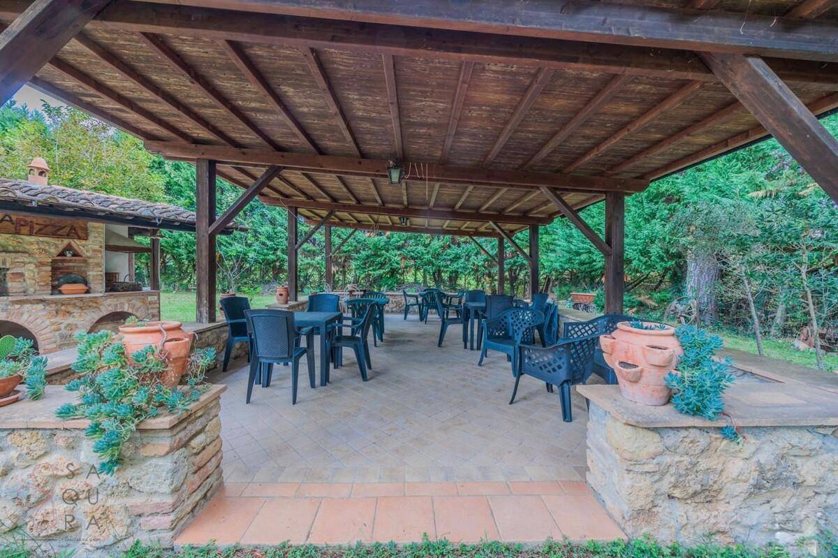 Überdachte Terrasse mit Sitzgelegenheiten und einem traditionellen Pizzaofen im Grünen.