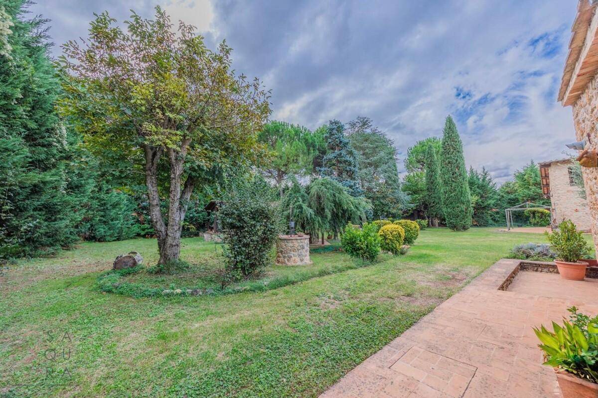 Gepflegter Gartenbereich mit Rasen, Bäumen und einem Steinbrunnen, ideal zum Entspannen im Freien.