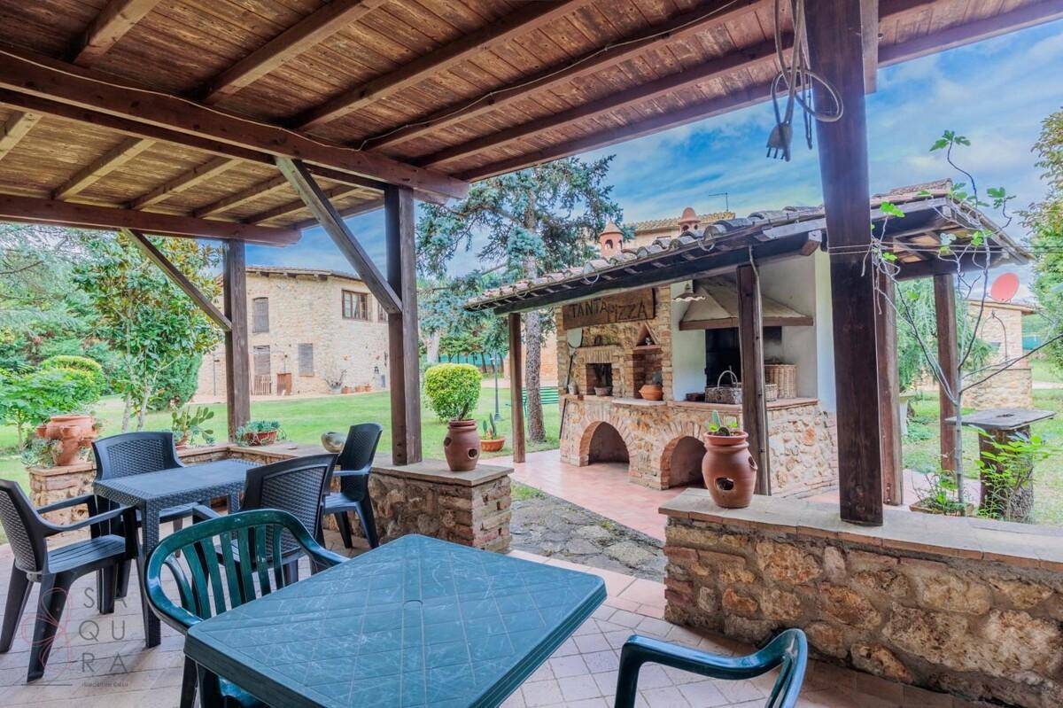 Blick von der überdachten Terrasse auf den Garten, den Pizzaofen und das Haupthaus.