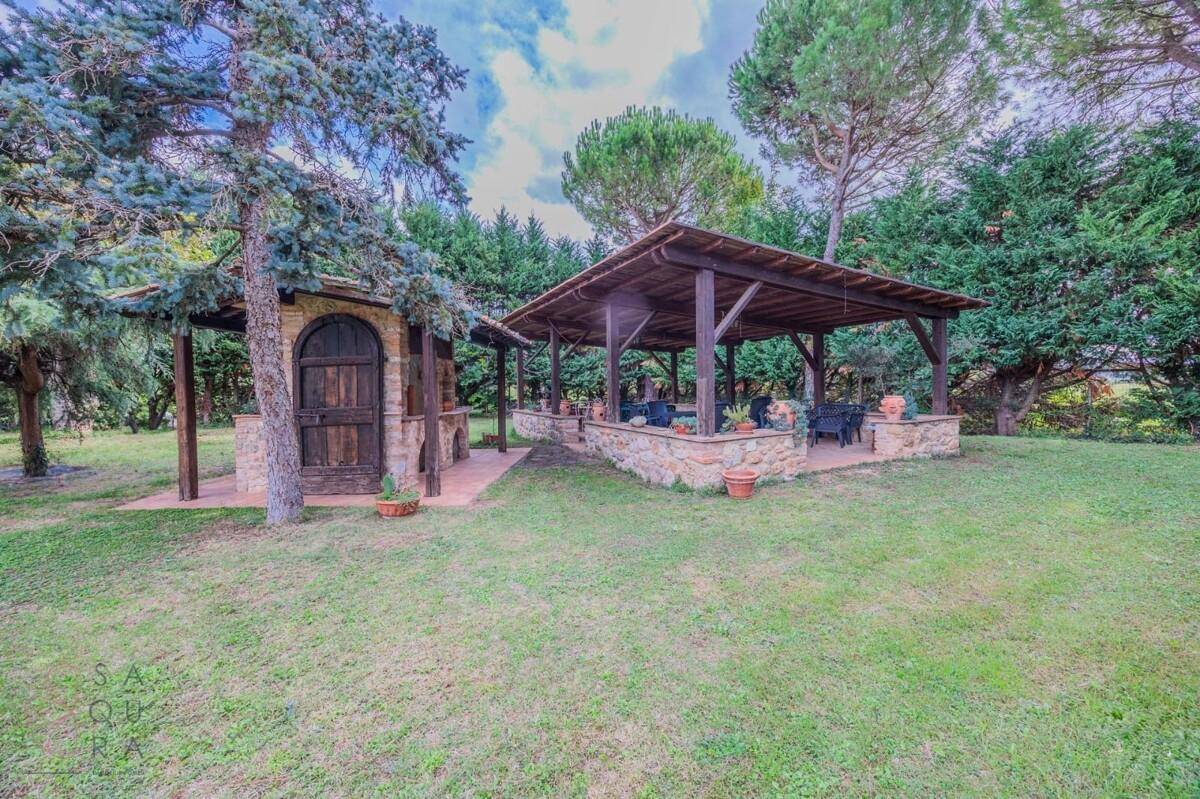 Weitläufiger Gartenbereich mit überdachtem Sitzplatz und einem charmanten Steingebäude.