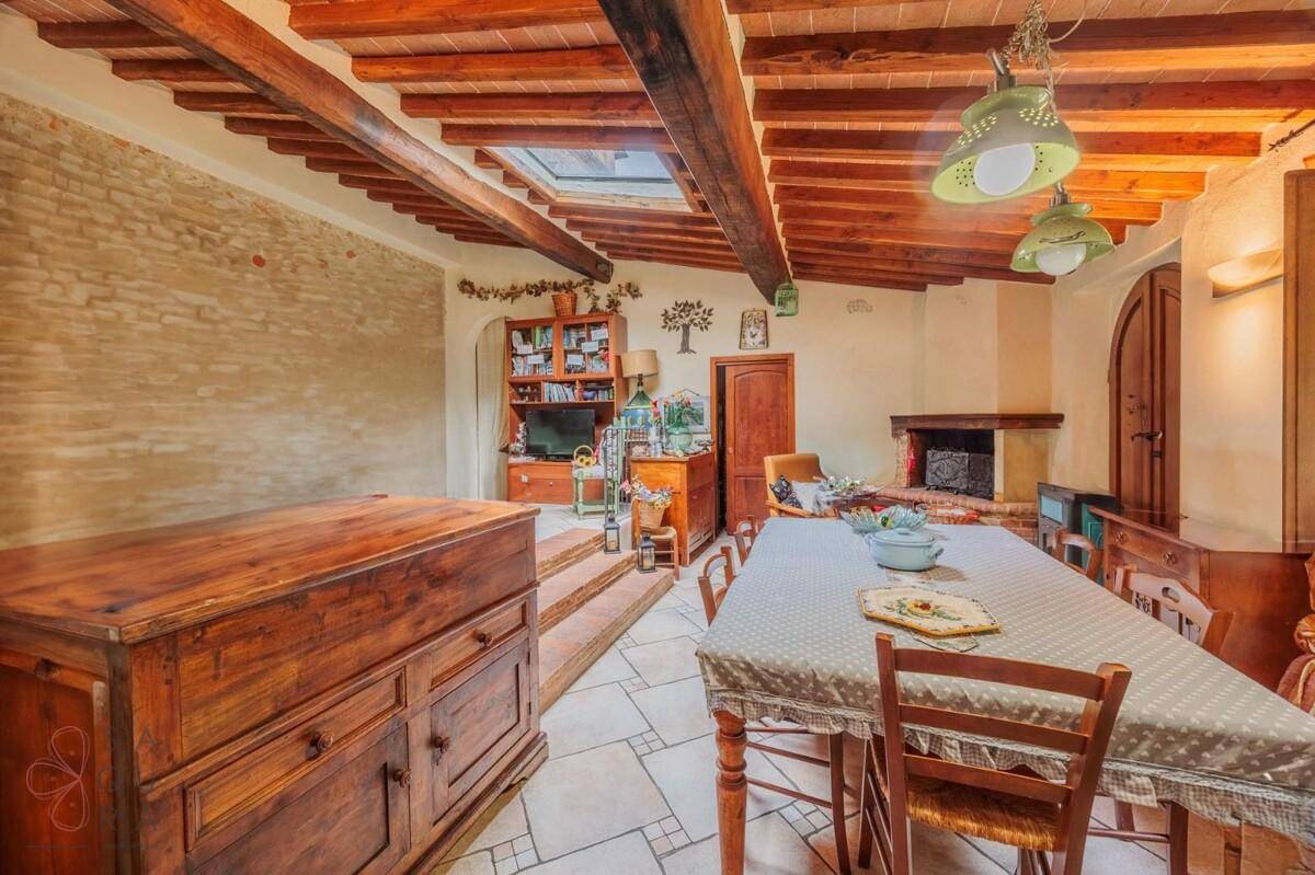 Essbereich mit langem Tisch, gefliestem Boden, Kamin und sichtbaren Deckenbalken sowie Oberlicht.