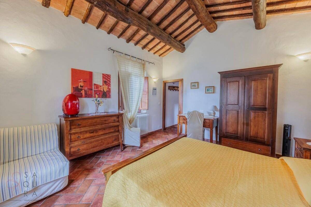 Schlafzimmer mit Doppelbett, Holzkommode und kleinem Sofa, unter rustikalen Deckenbalken.