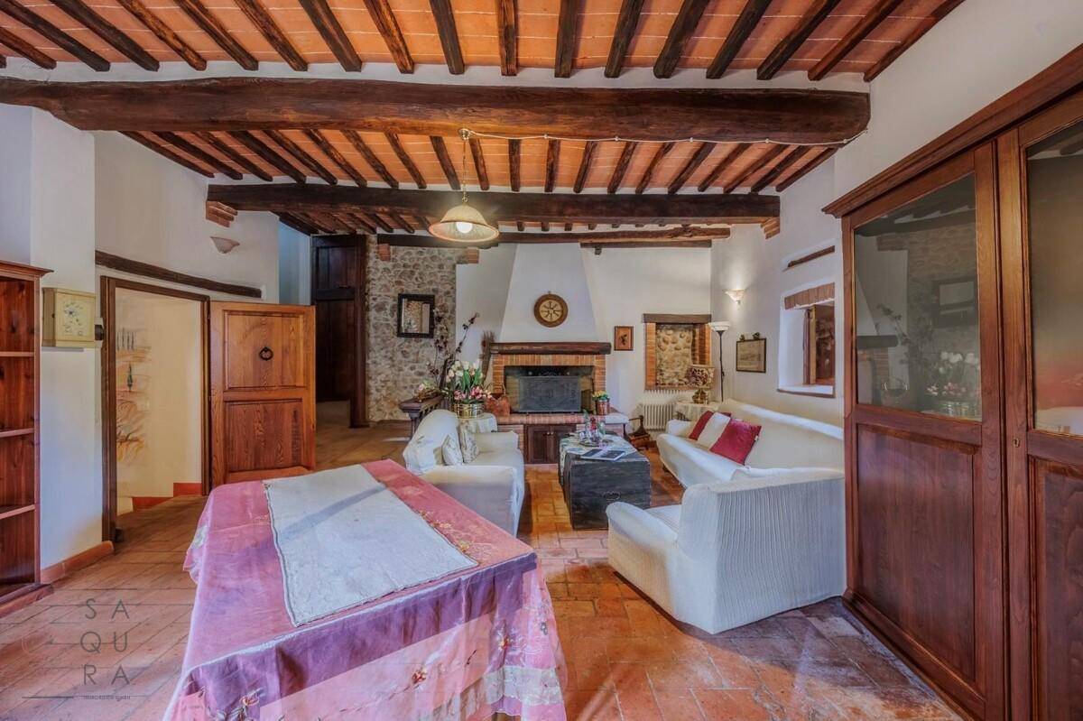 Ansicht des Wohnzimmers mit Kamin, bequemen Sofas und rustikalen Holzbalken an der Decke.