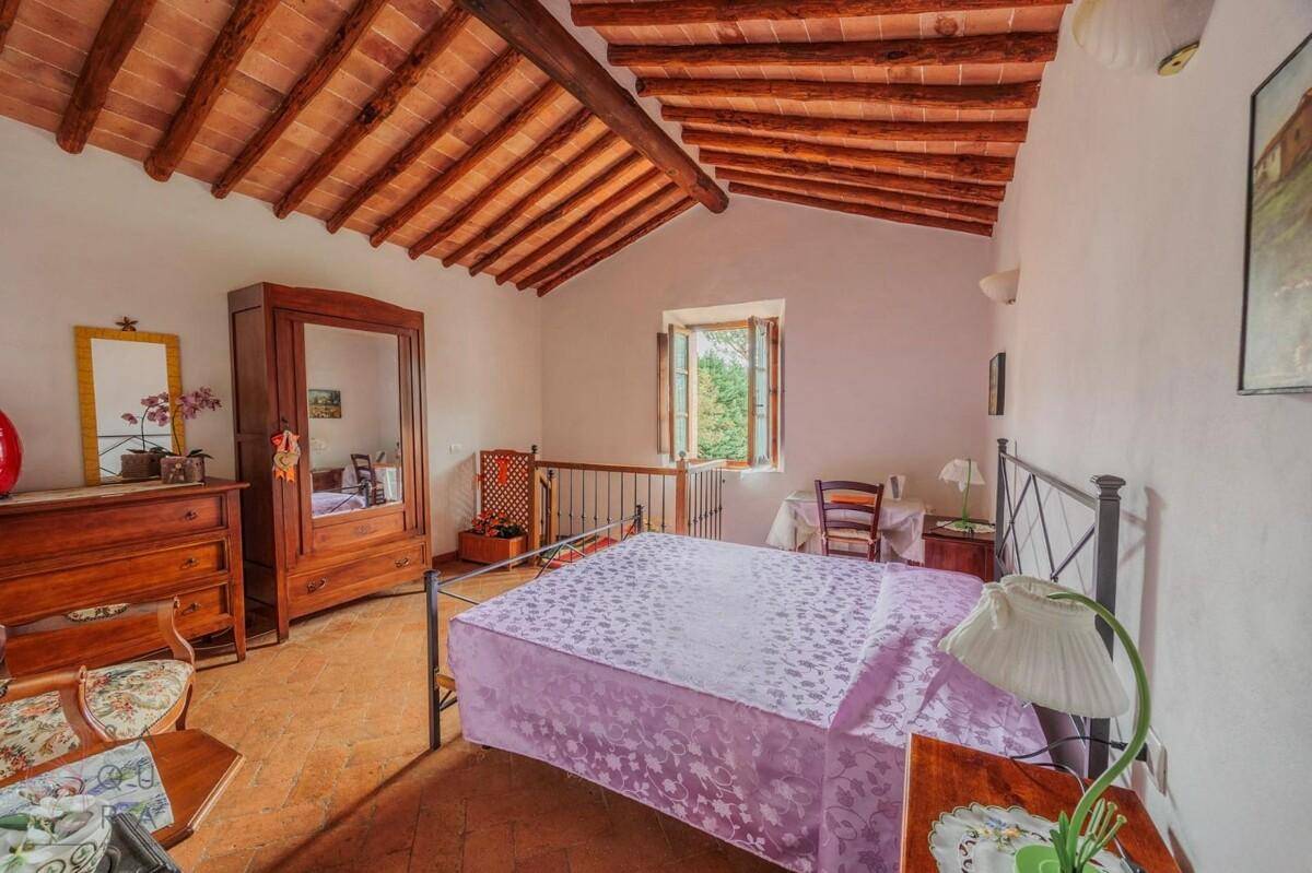 Schlafzimmer mit Doppelbett, Holzmöbeln, Terrakottaboden und sichtbaren Deckenbalken.