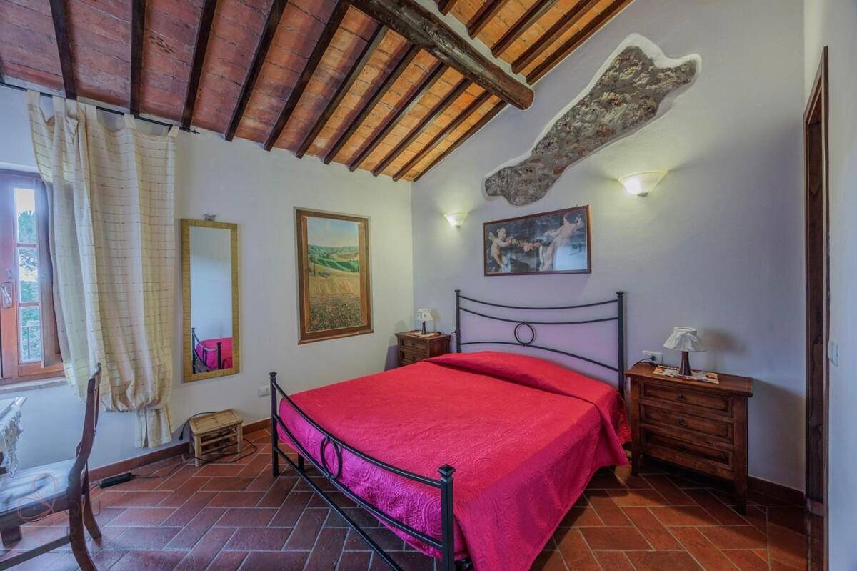 Schlafzimmer mit Doppelbett, Holzmöbeln und Fenster, mit Terrakottaboden und Holzbalkendecke.