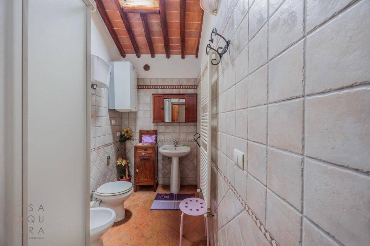 Badezimmer mit Fliesen, Duschkabine, WC, Bidet und Holzbalkendecke mit Dachfenster.
