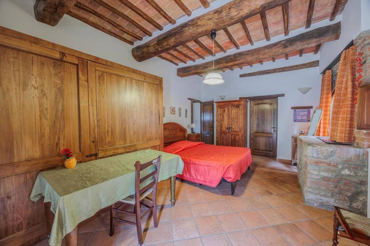 Schlafzimmer mit Doppelbett, Holzschrank und kleinem Schreibtisch, unter rustikalen Deckenbalken.