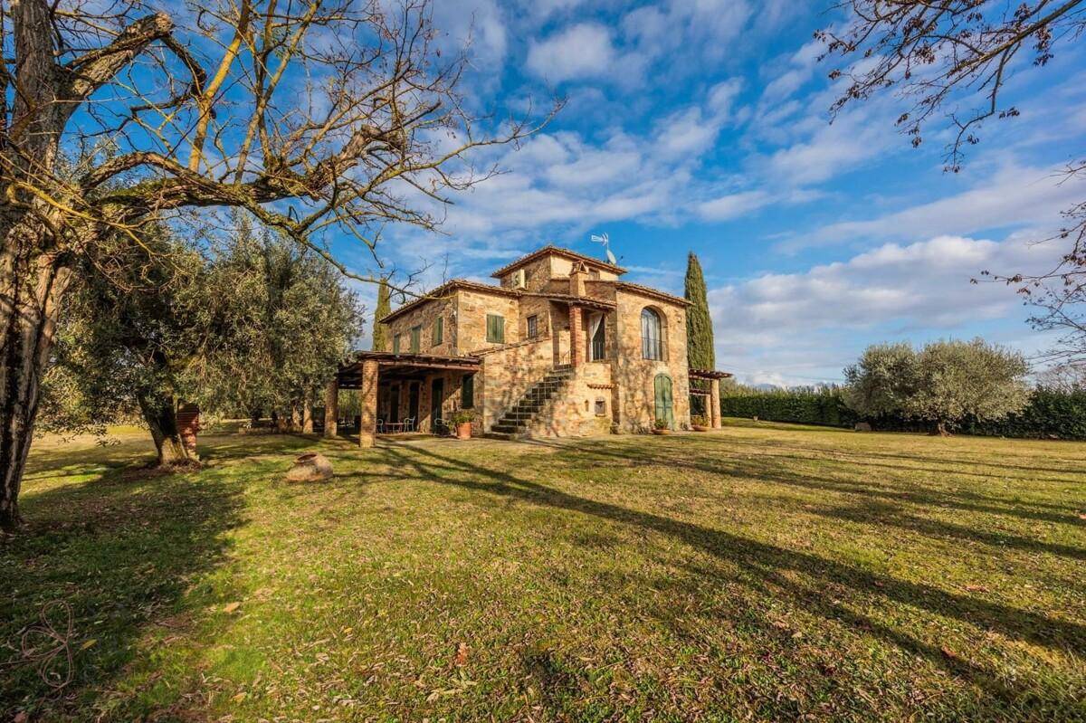 Weitläufige Ansicht des traditionellen Steinhauses mit großem Garten und alten Bäumen unter blauem Himmel.