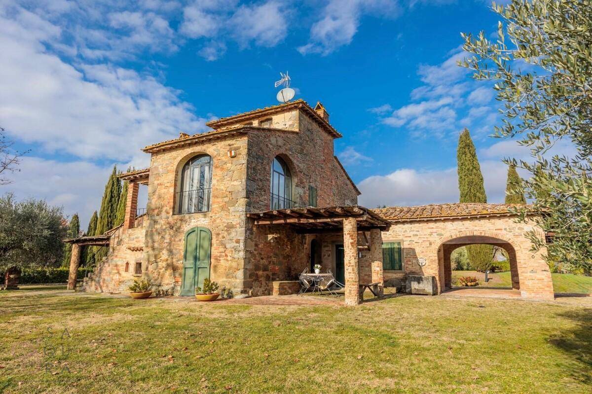 Rustikales Steinhaus mit überdachter Terrasse und einem Bogen, umgeben von mediterraner Vegetation.
