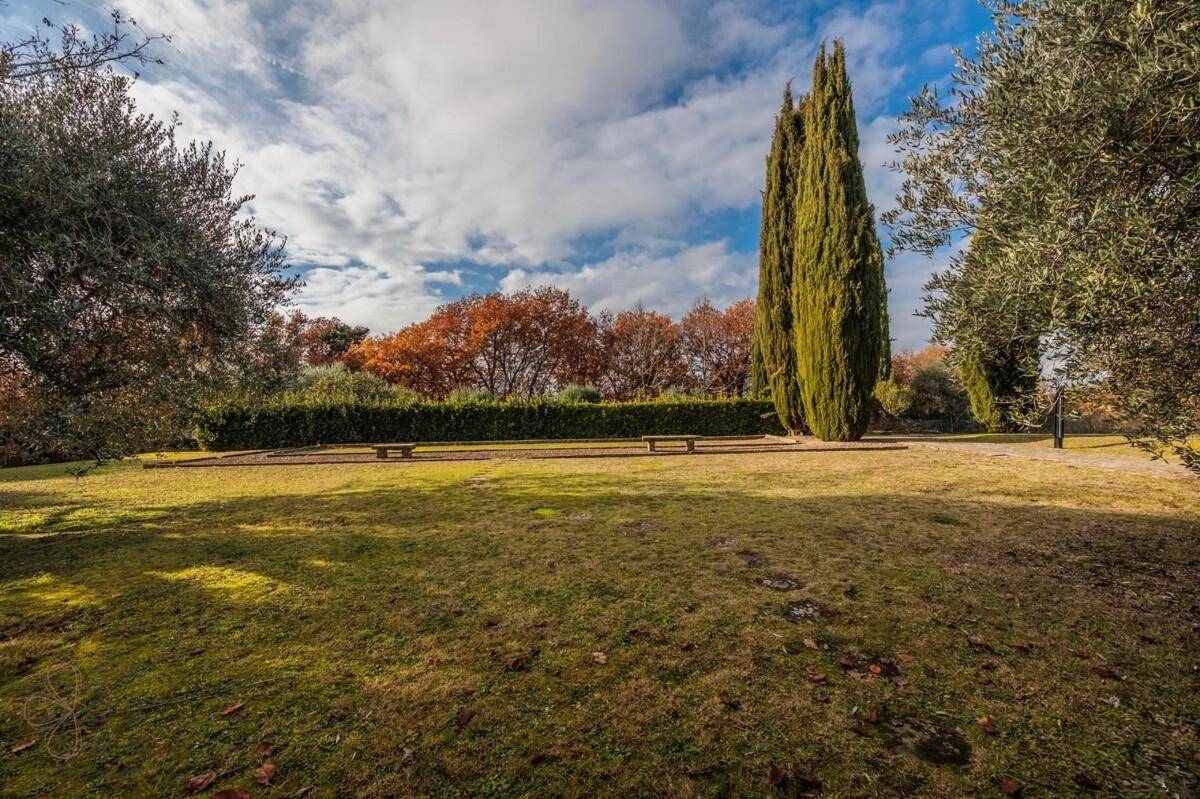 Großer, gepflegter Garten mit Rasenflächen, Bänken und hohen Zypressen unter blauem Himmel.