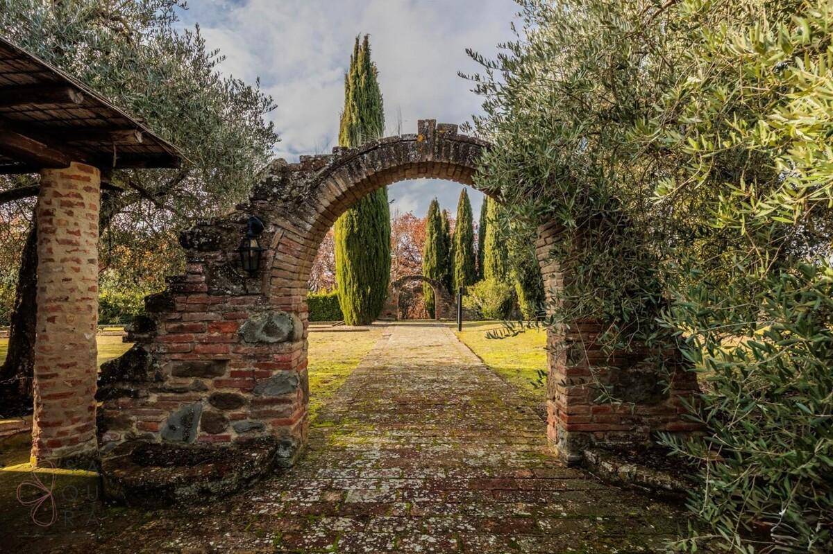 Malerischer Steinbogen im Garten, der einen Weg zu weiteren Zypressen und der Landschaft öffnet.