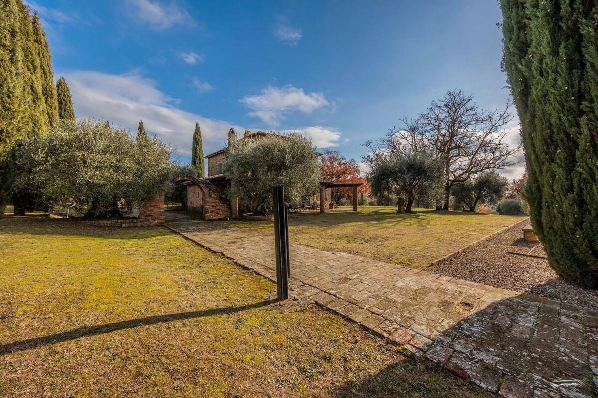 Gartenweg aus Ziegeln und Kies, umgeben von Olivenbäumen und Zypressen, mit Blick auf das Haus.
