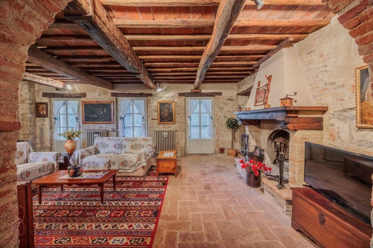 Geräumiges Wohnzimmer mit Kamin, Holzbalkendecke, Steinwänden und traditionellem Teppich.