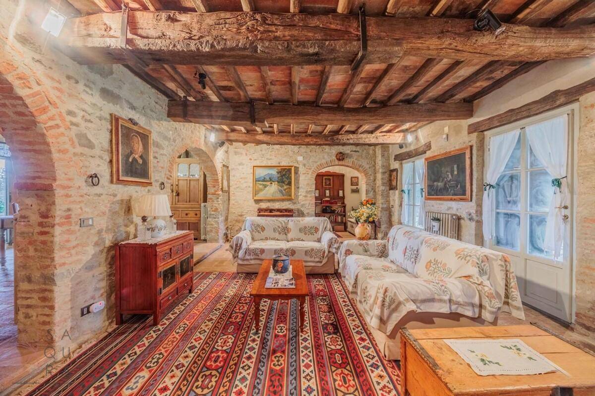 Weitläufiges Wohnzimmer mit Steinwänden, Holzbalkendecke und farbenfrohem Teppich.