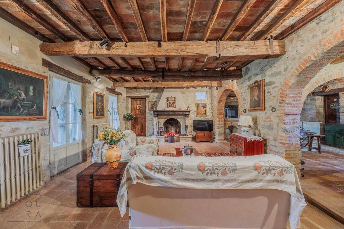 Großes Wohnzimmer mit Kamin, Holzbalkendecke und rustikalen Möbeln, offen zum Essbereich.