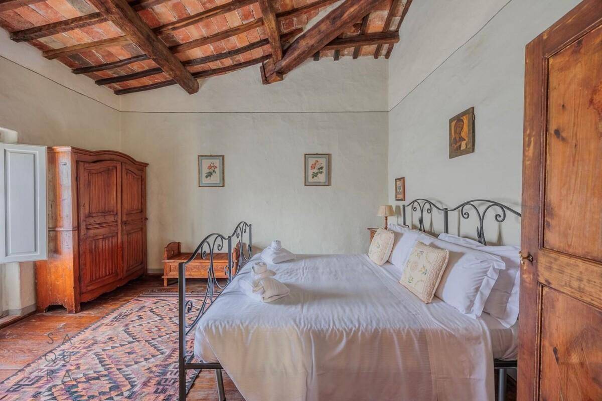 Schlafzimmer mit schmiedeeisernem Bett, Holzboden und Holzbalkendecke, strahlt einen rustikalen Charme aus.
