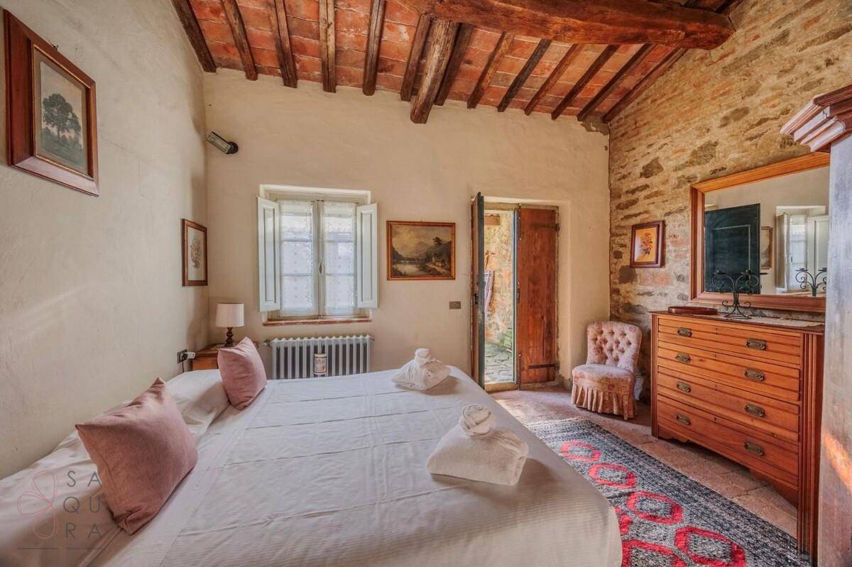 Schlafzimmer mit Terrakottaboden, Holzbalkendecke und einem antiken Schminktisch, bietet Zugang zu einem Außenbereich.