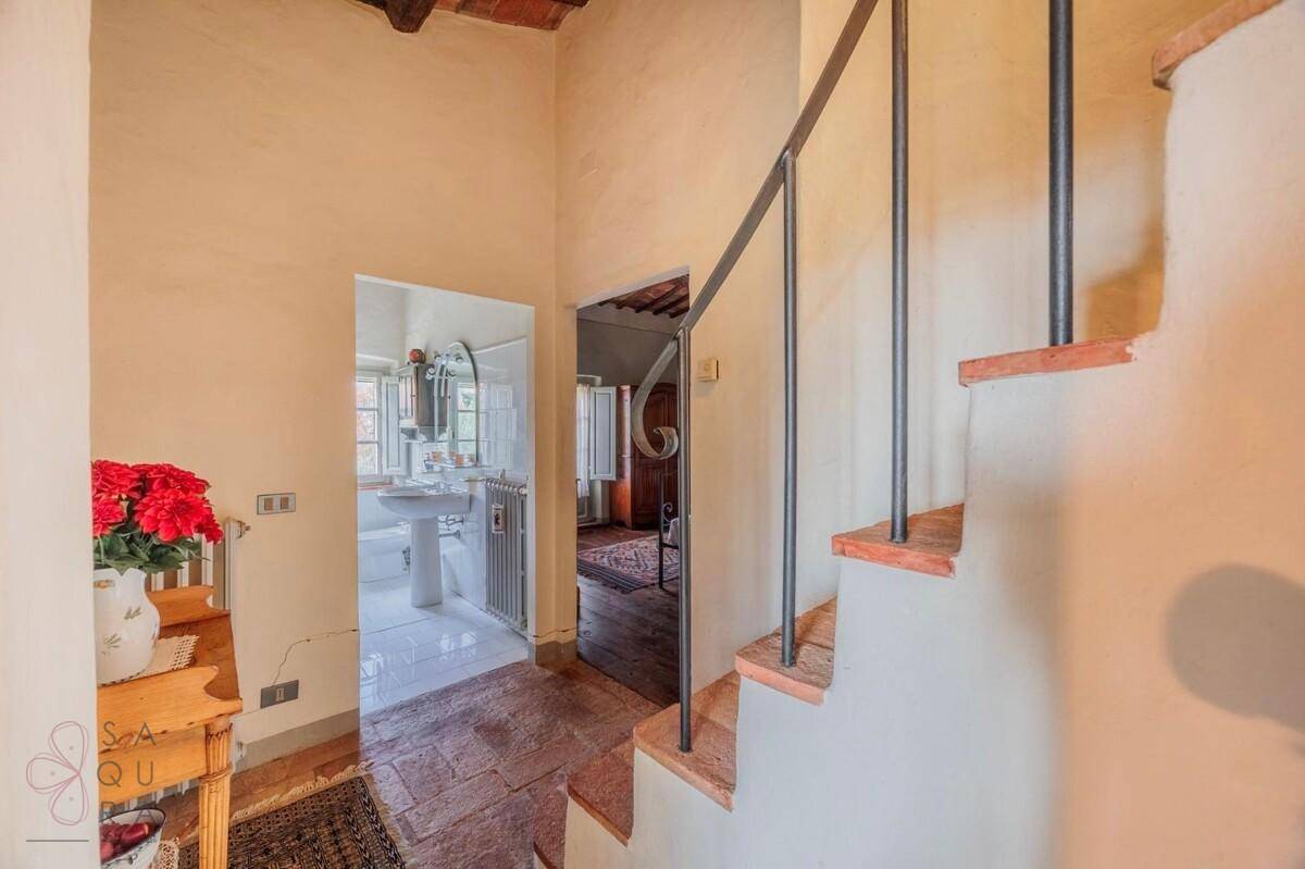 Flur mit Terrakottaboden und Treppe, die zu den oberen Etagen führt, mit Blick auf ein Badezimmer.