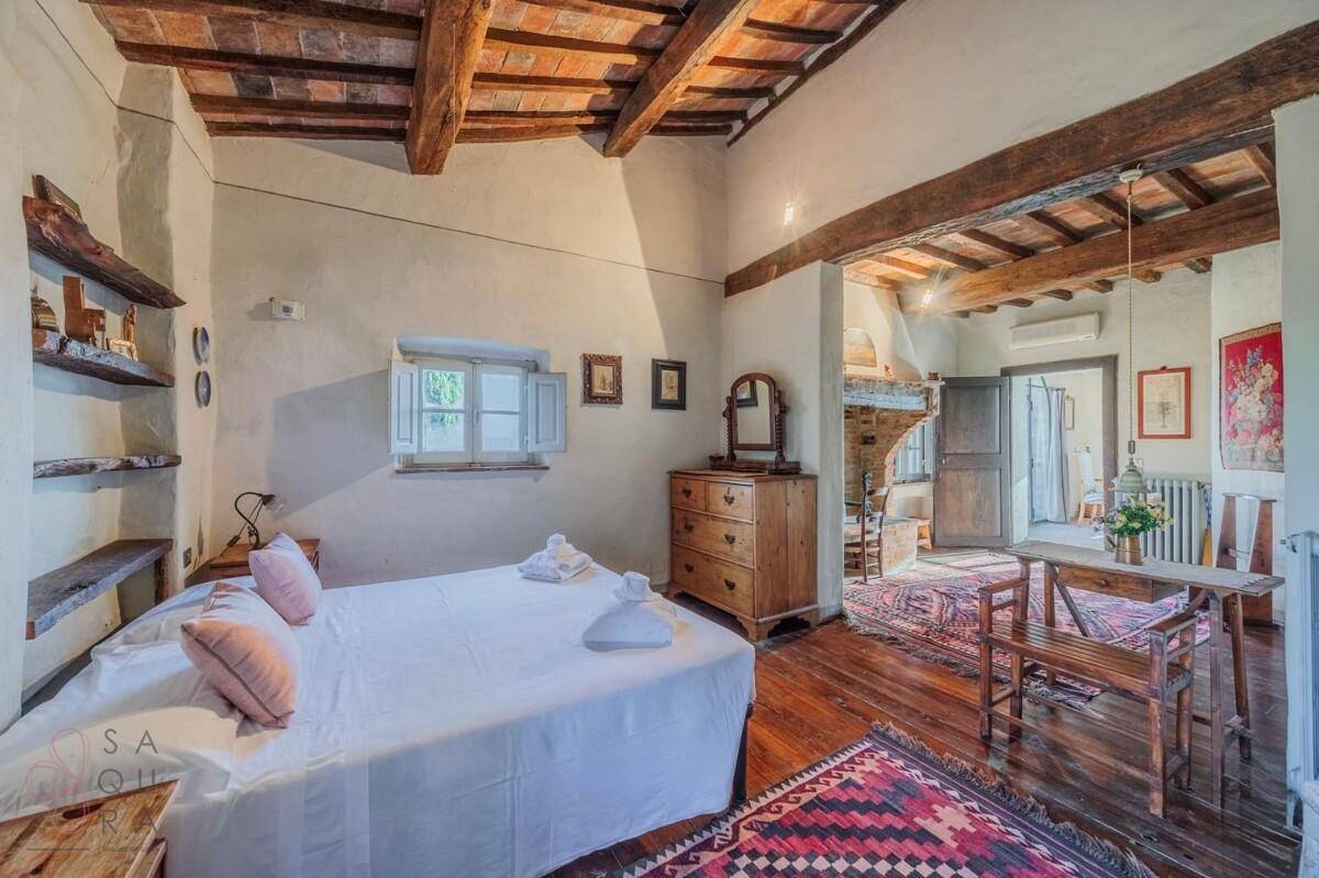 Schlafzimmer mit Holzbalkendecke und Holzboden, verbunden mit einem weiteren Raum, der den rustikalen Stil fortsetzt.