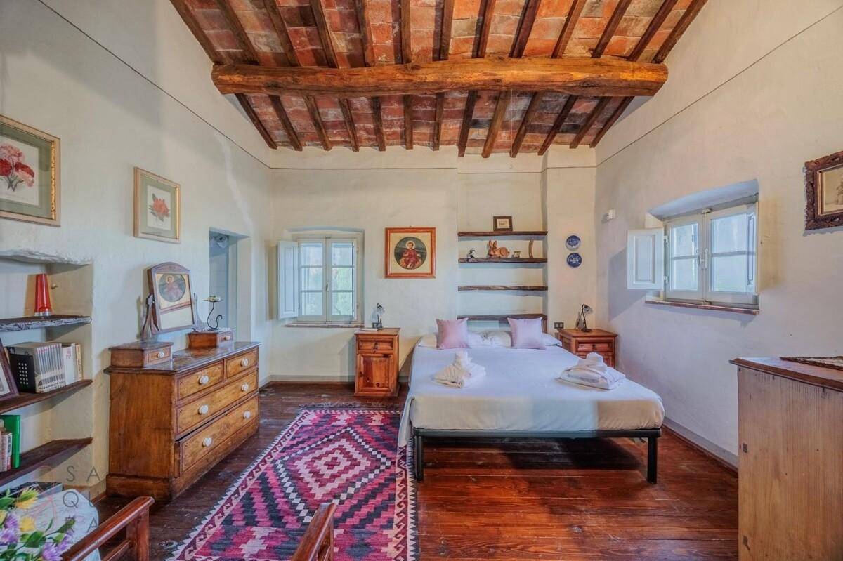 Helles Schlafzimmer mit Holzbalkendecke, Holzboden und traditionellen Möbeln, darunter eine Kommode und Nachttische.