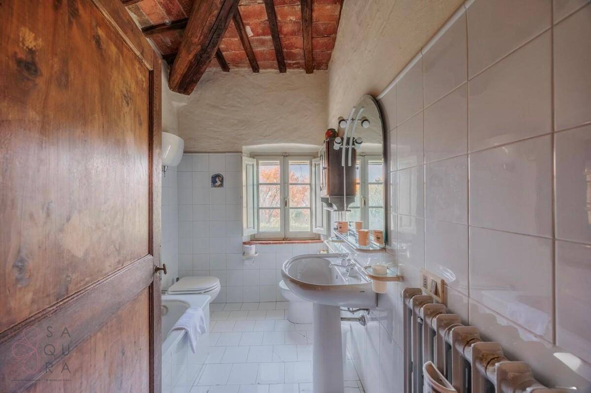 Badezimmer mit Waschbecken, WC und Bidet, gefliest mit weißen Fliesen und einem Fenster für natürliche Belüftung.
