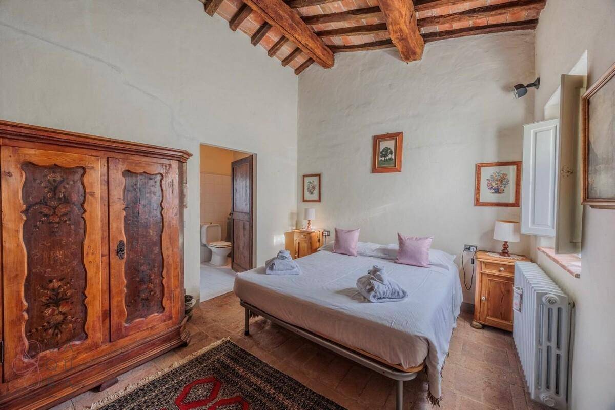 Schlafzimmer mit Holzbalkendecke, Terrakottaboden und einem antiken Kleiderschrank, mit Zugang zum Badezimmer.