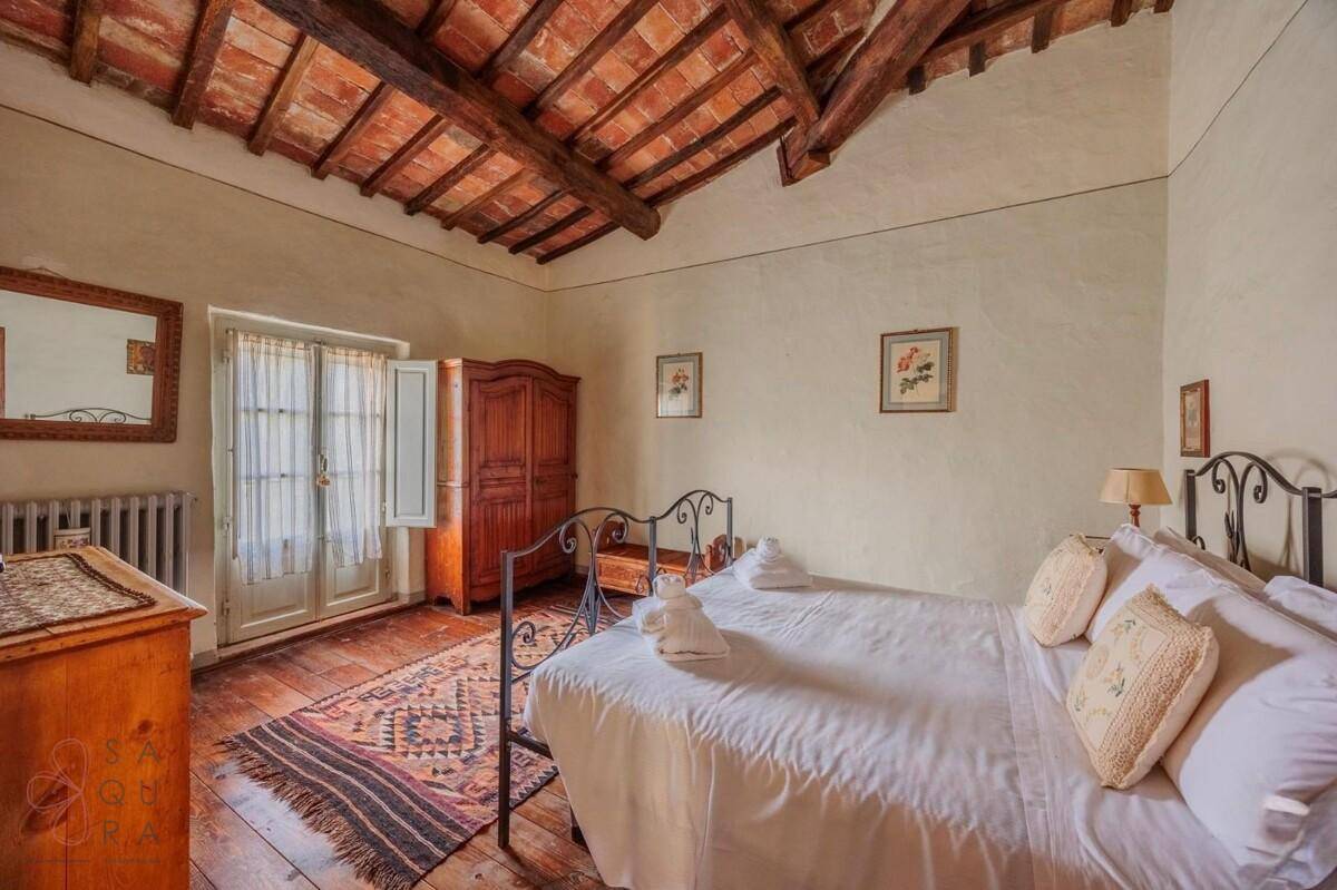 Schlafzimmer mit Holzbalkendecke, Holzboden und französischen Türen, die viel natürliches Licht hereinlassen.