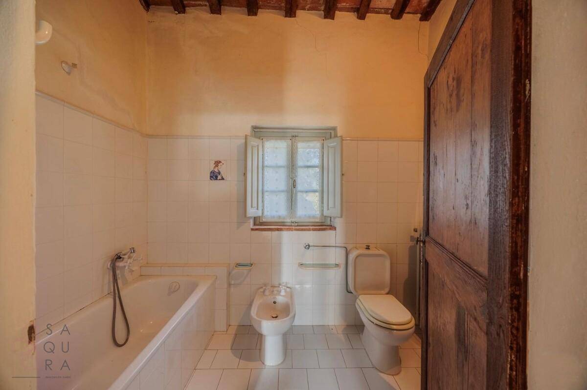 Badezimmer mit Badewanne, Bidet und WC, gefliest mit weißen Fliesen und einem Fenster für Tageslicht.
