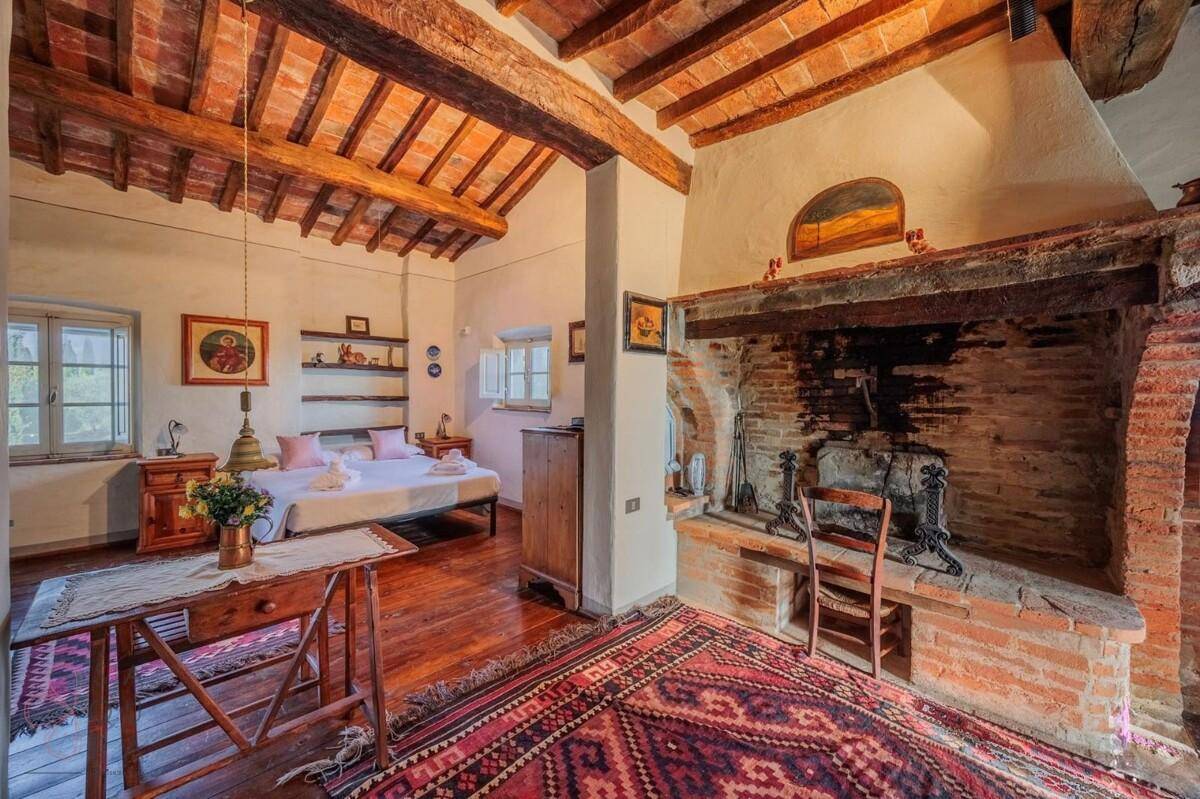 Geräumiges Schlafzimmer mit Holzbalkendecke, Kamin und Holzboden, bietet eine warme und einladende Atmosphäre.