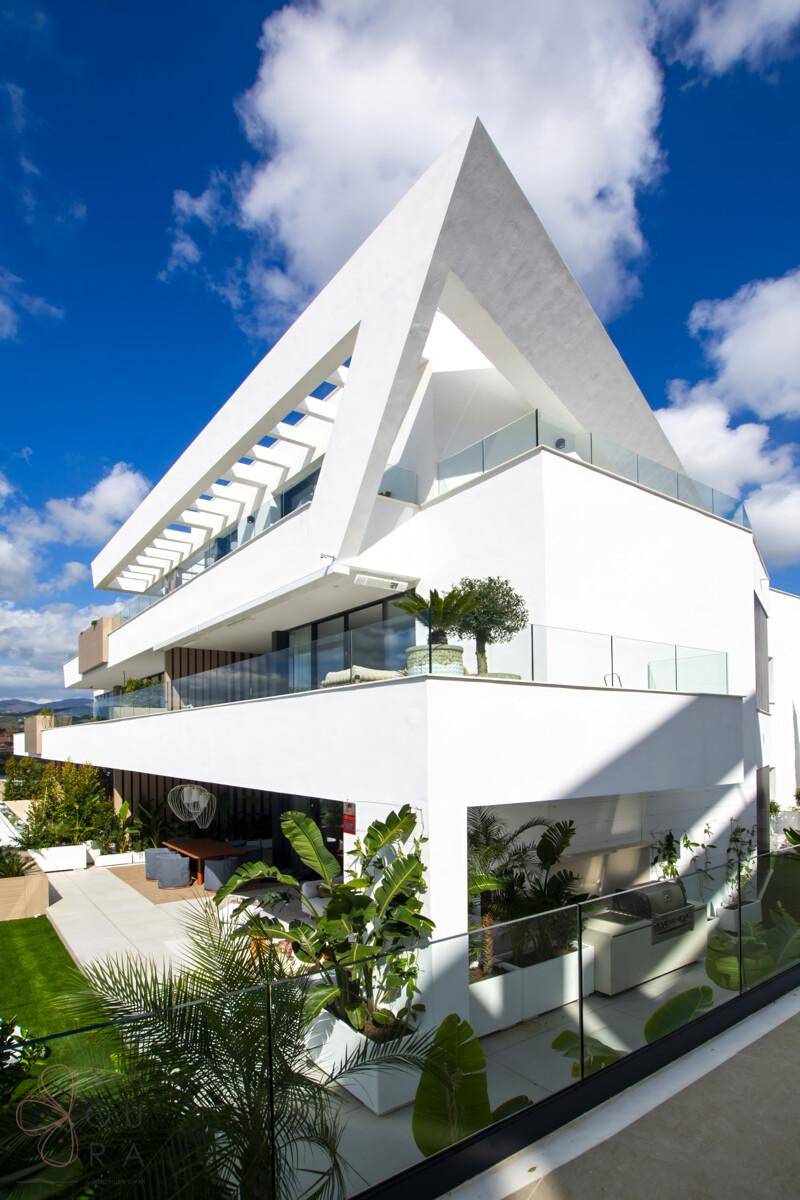 Moderne weiße Architektur mit markanten Linien, großen Balkonen und Glasgeländern unter blauem Himmel.