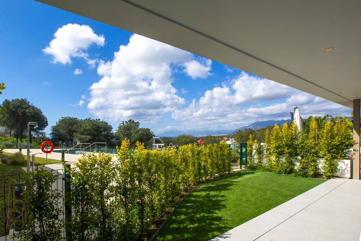 Überdachte Terrasse mit Blick auf eine gepflegte Rasenfläche, Hecken und die umliegende Landschaft.