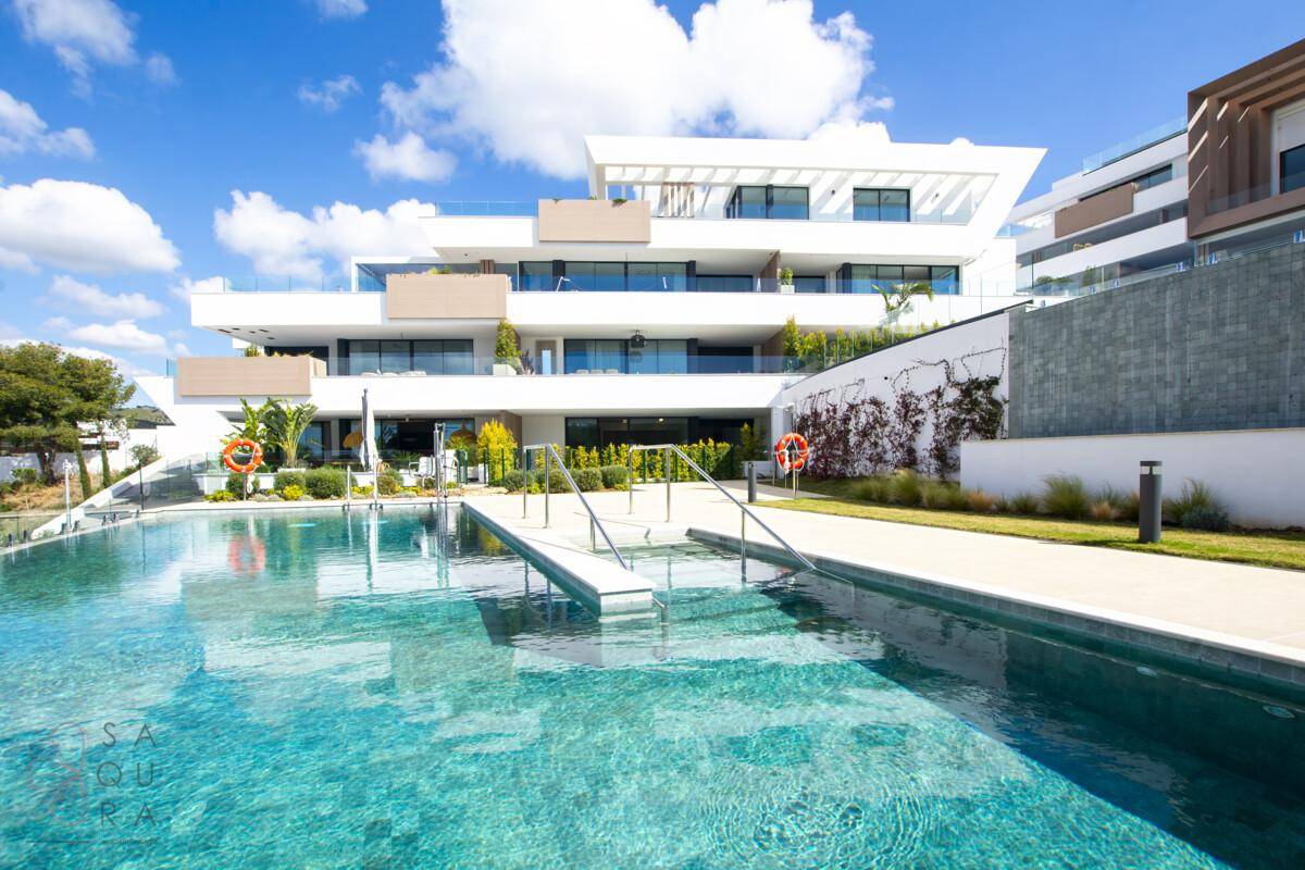 Luxuriöser Apartmentkomplex mit großem Gemeinschaftspool und gepflegter Gartenanlage unter blauem Himmel.